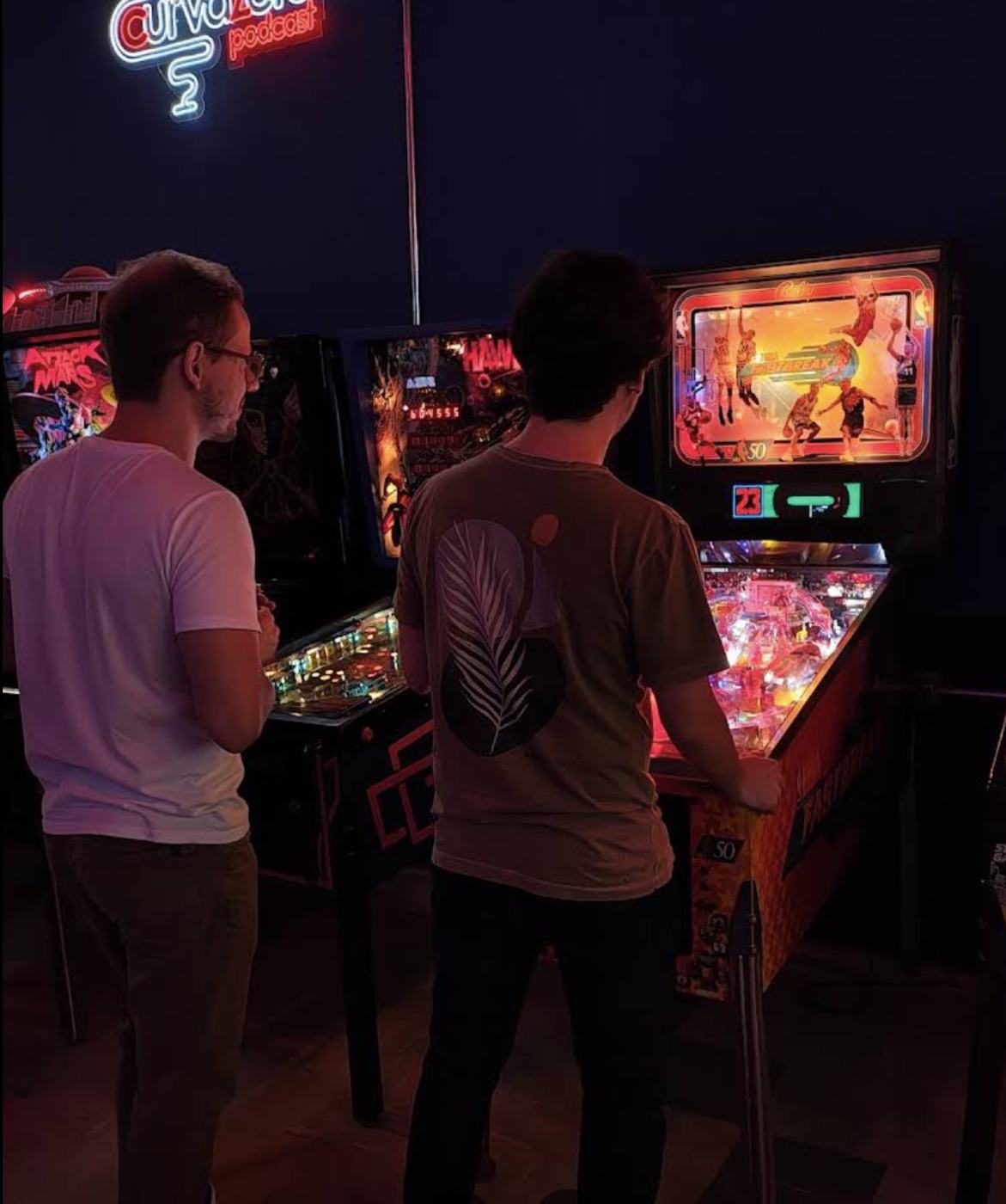 Dupla jogando pinball na Base Experience à noite